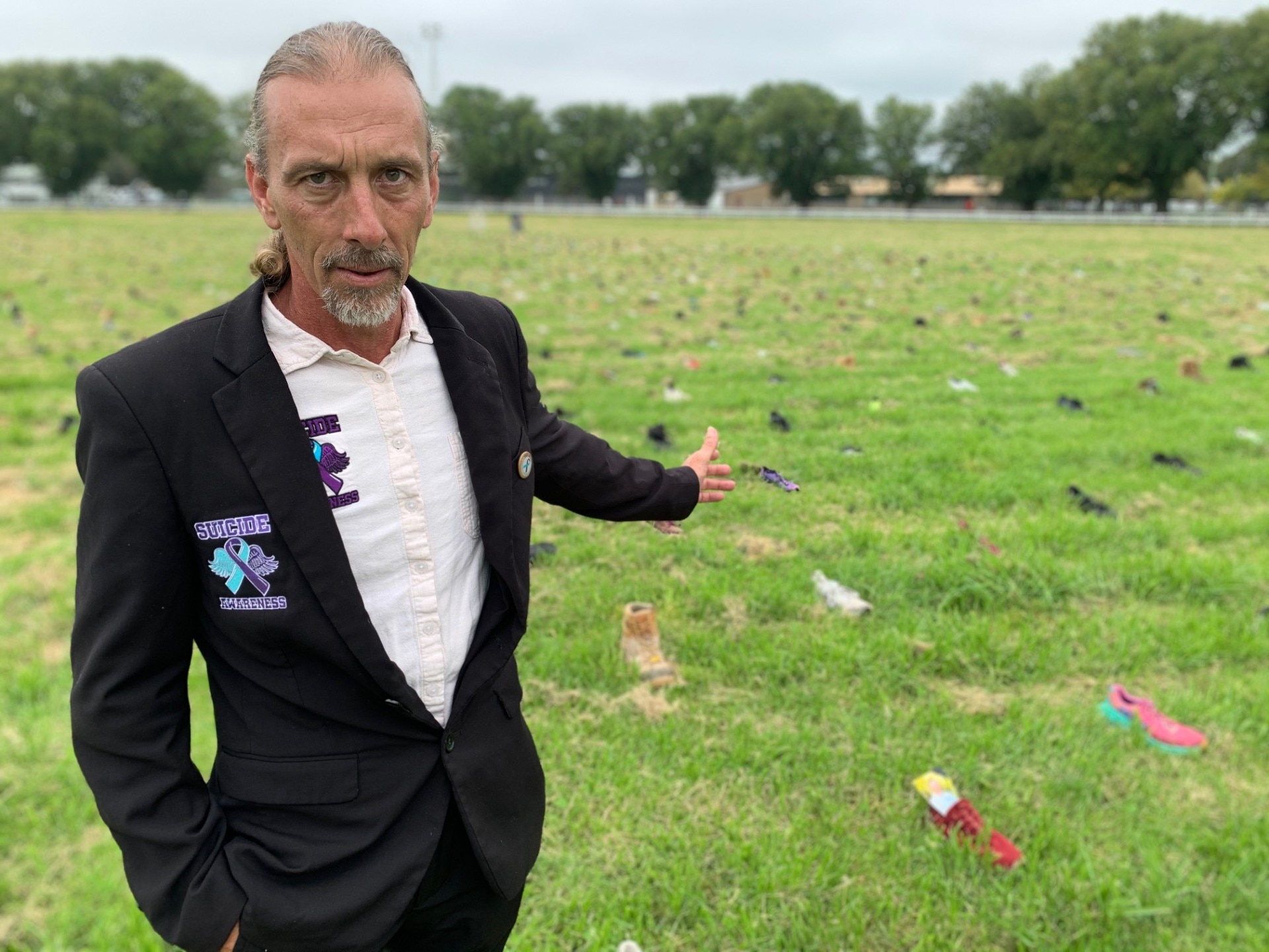 Man in dark jacket stands in front of a sea of shoes.