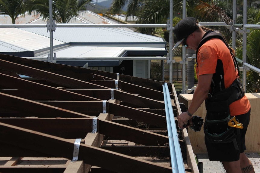 Carpentry apprentice Emily Bailey uses a power drill to work on a roofing project, high up on scaffolding.