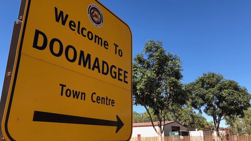 A roadside sign in the outback  reads 'Welcome to Doomadgee'.