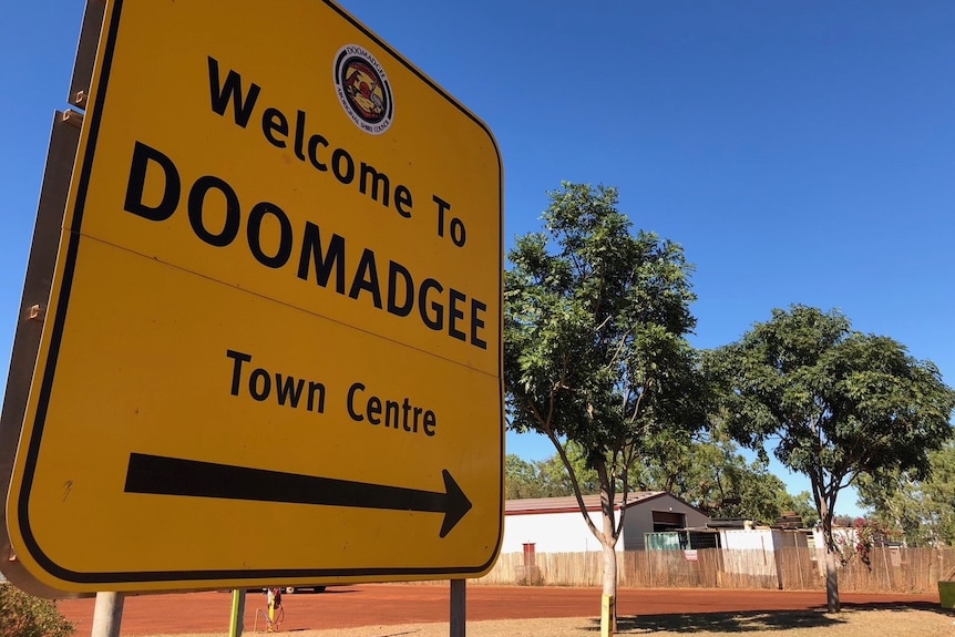 A roadside sign in the outback reads 'Welcome to Doomadgee'.