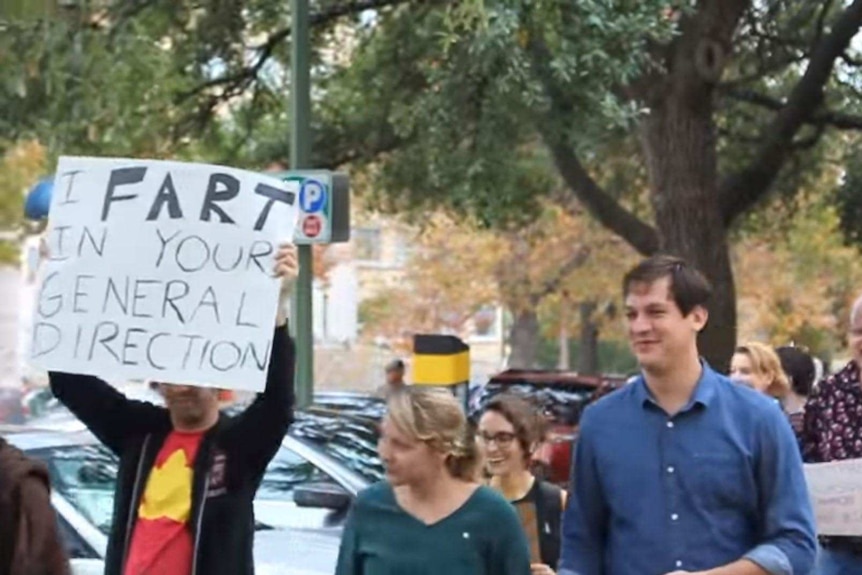 A protester holds a sign saying "I fart in your general direction".