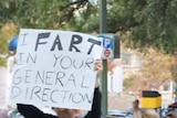 A protester holds a sign saying "I fart in your general direction".