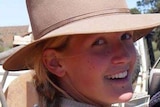 A woman wearing a cowboy hat looks back over her shoulder at the camera