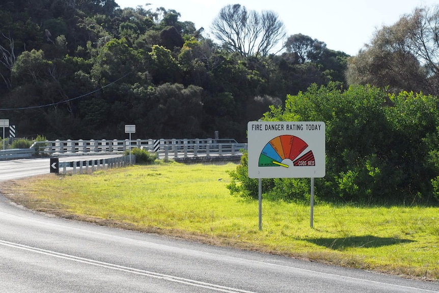 A fire danger rating sign beside a road and trees points to a low to moderate risk.