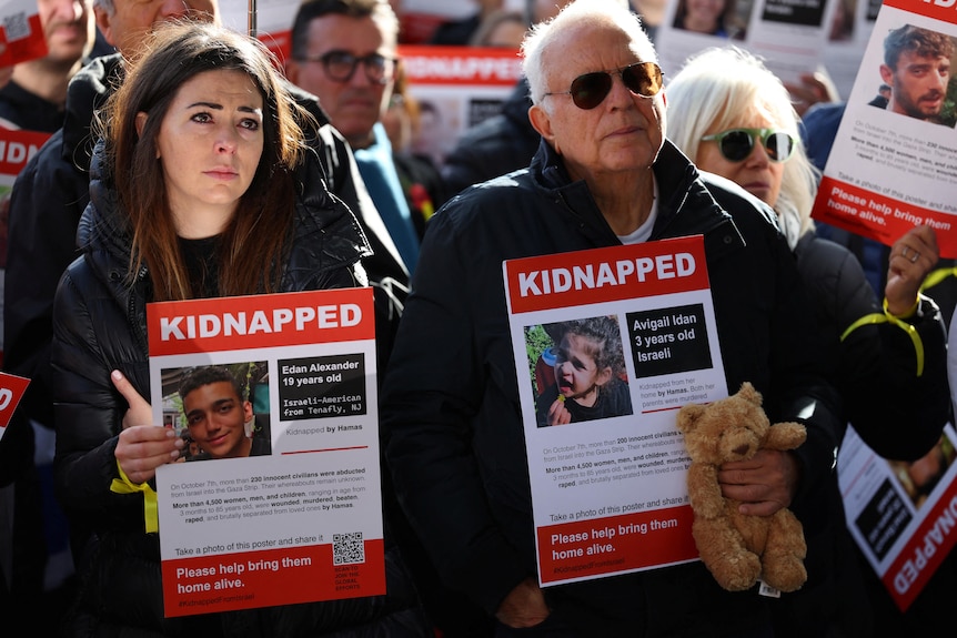a woman looking distraught and a man stand side by side in a crowd, holding up signs that say "kidnapped"