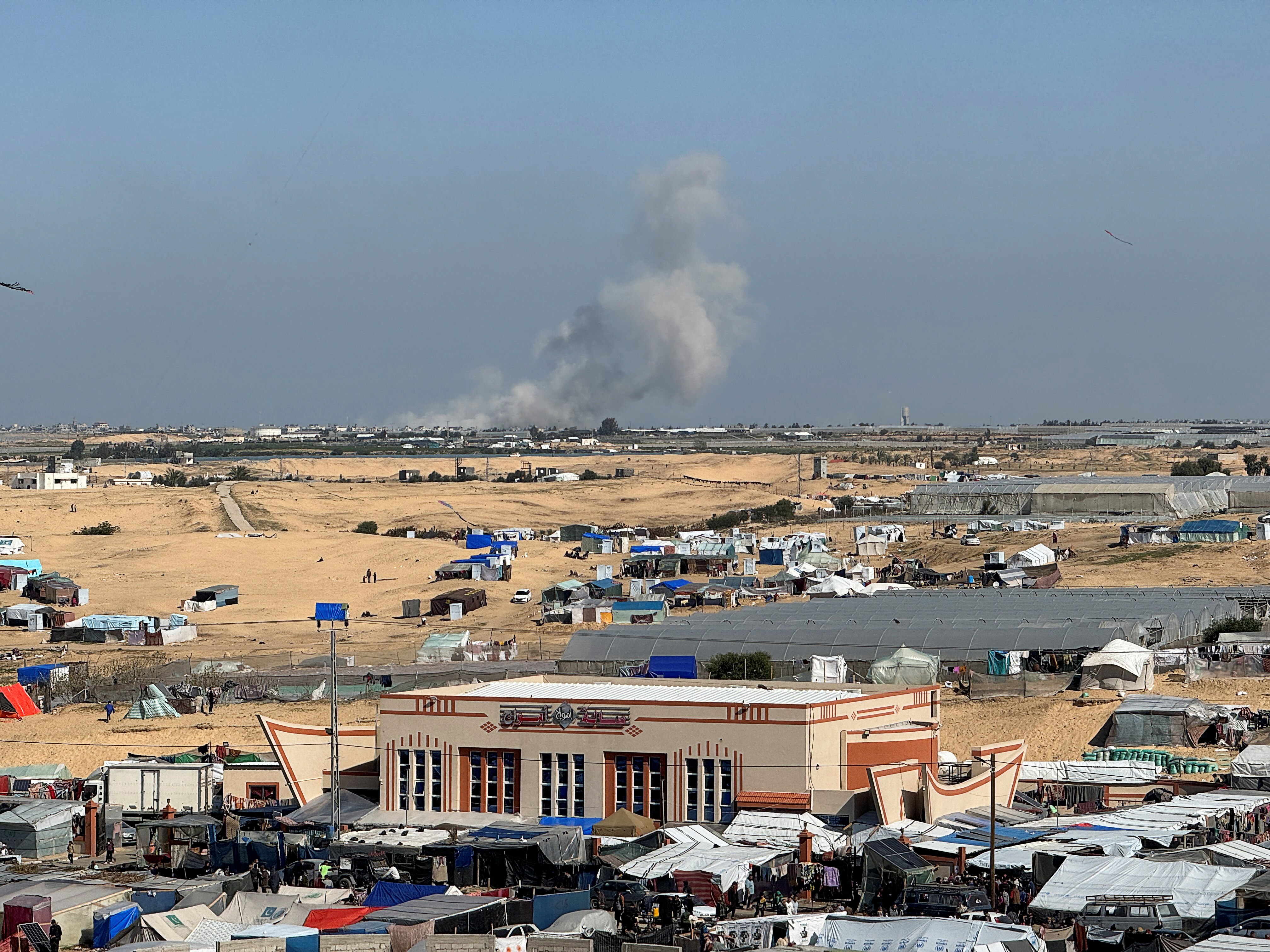 smoke rises during the daytime on a clear sky over tents in a camp, 