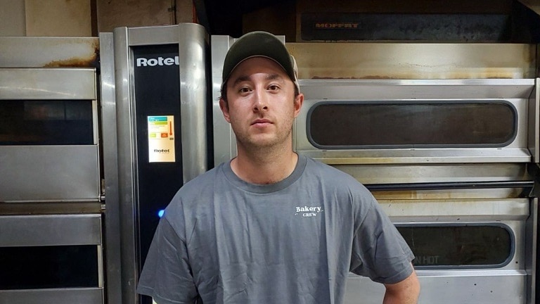 Man wearing cap and grey t-shirt standing in front of electric ovens