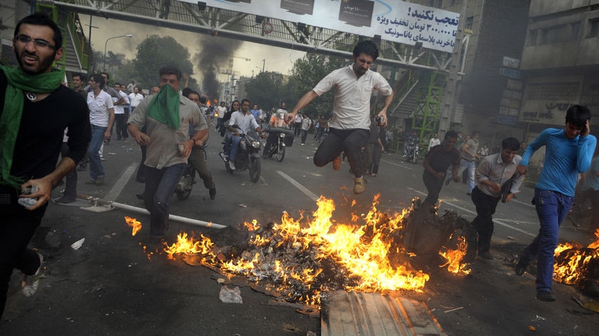 Iranian protesters jump and run over a fire during protests in Tehran