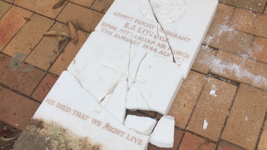 A white, marble headstone commemorating a WWII veteran lies in pieces on the ground.