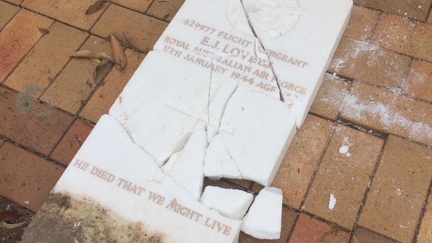 A white, marble headstone commemorating a WWII veteran lies in pieces on the ground.