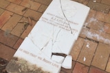 A white, marble headstone commemorating a WWII veteran lies in pieces on the ground.