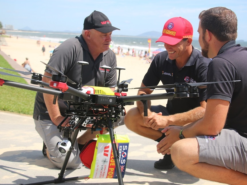 Three men looking at a large drone on the beach.