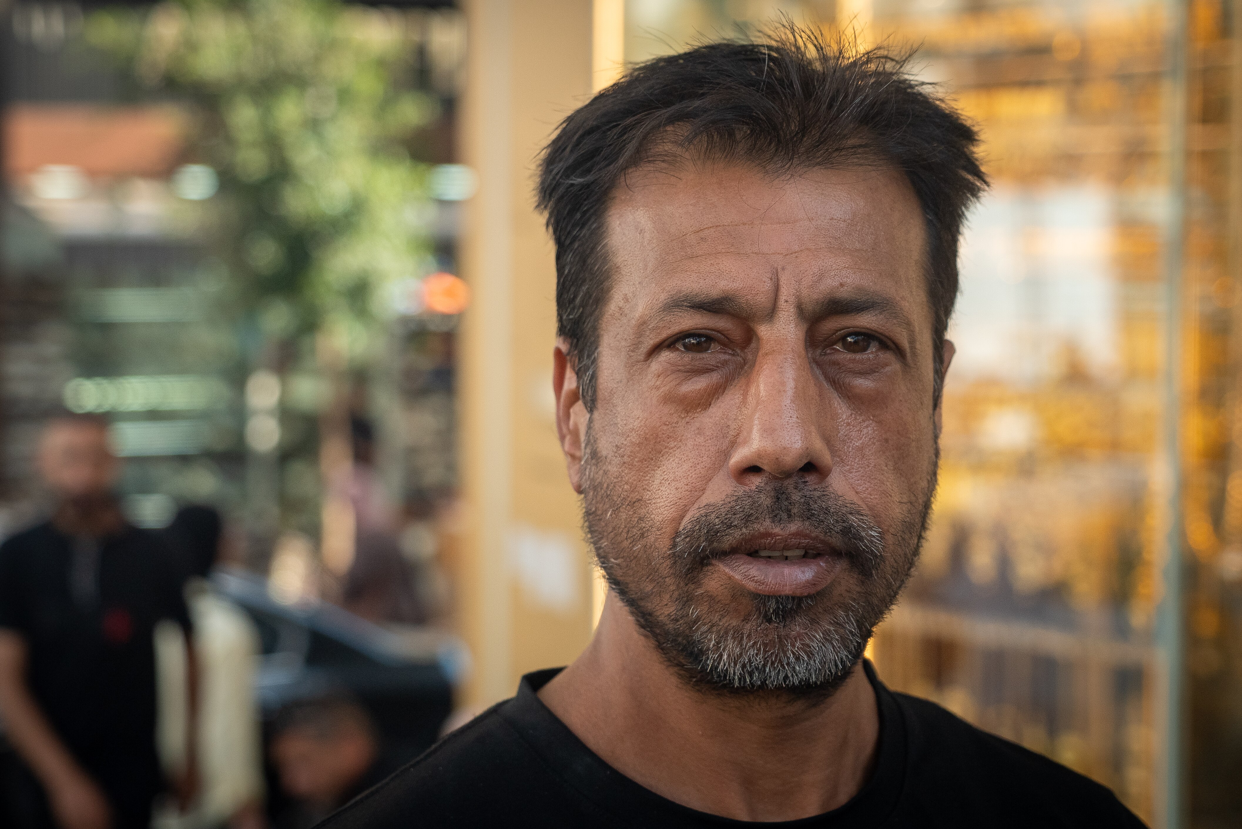 A man with short black hair and a salt and pepper beard furrows his brow. 