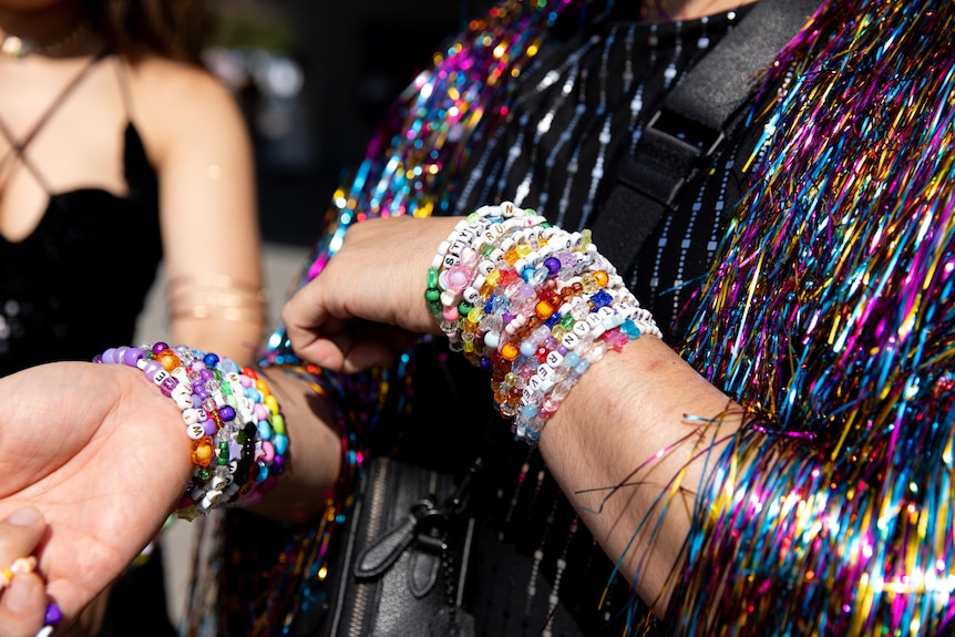 A close up of a person wearing several beaded friendship bracelets and a colourful shimmery jacket