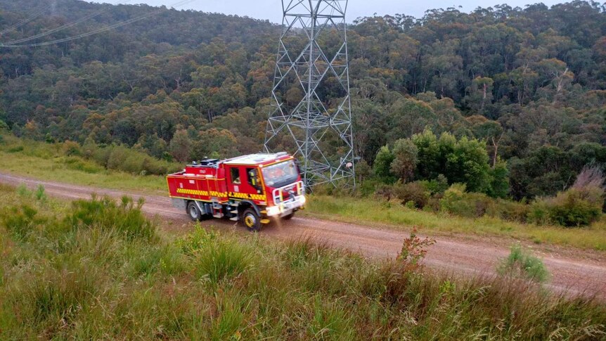 A fire truck traverses a dirt track in rugged bushland.