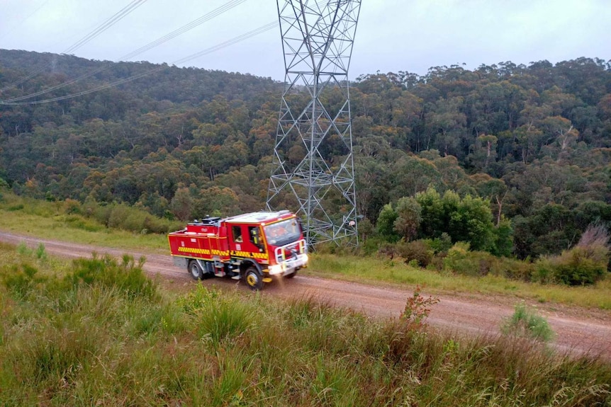 A fire truck traverses a dirt track in rugged bushland.