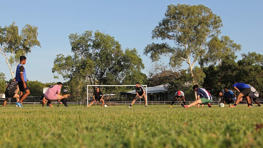 A semi-circle of soccer players doing warm-up stretches on the playing field.