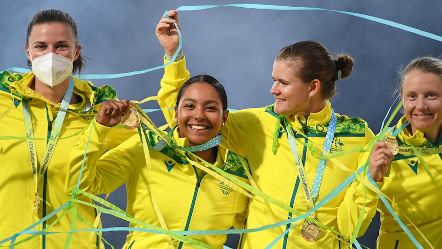Australian cricketers stand arm in arm with their medals as streamers fly at the gold medal game at the Commonwealth Games.