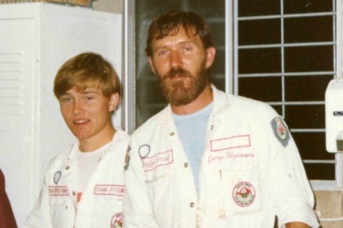A photo of a teenager and his father wearing white firefighter jumpsuits