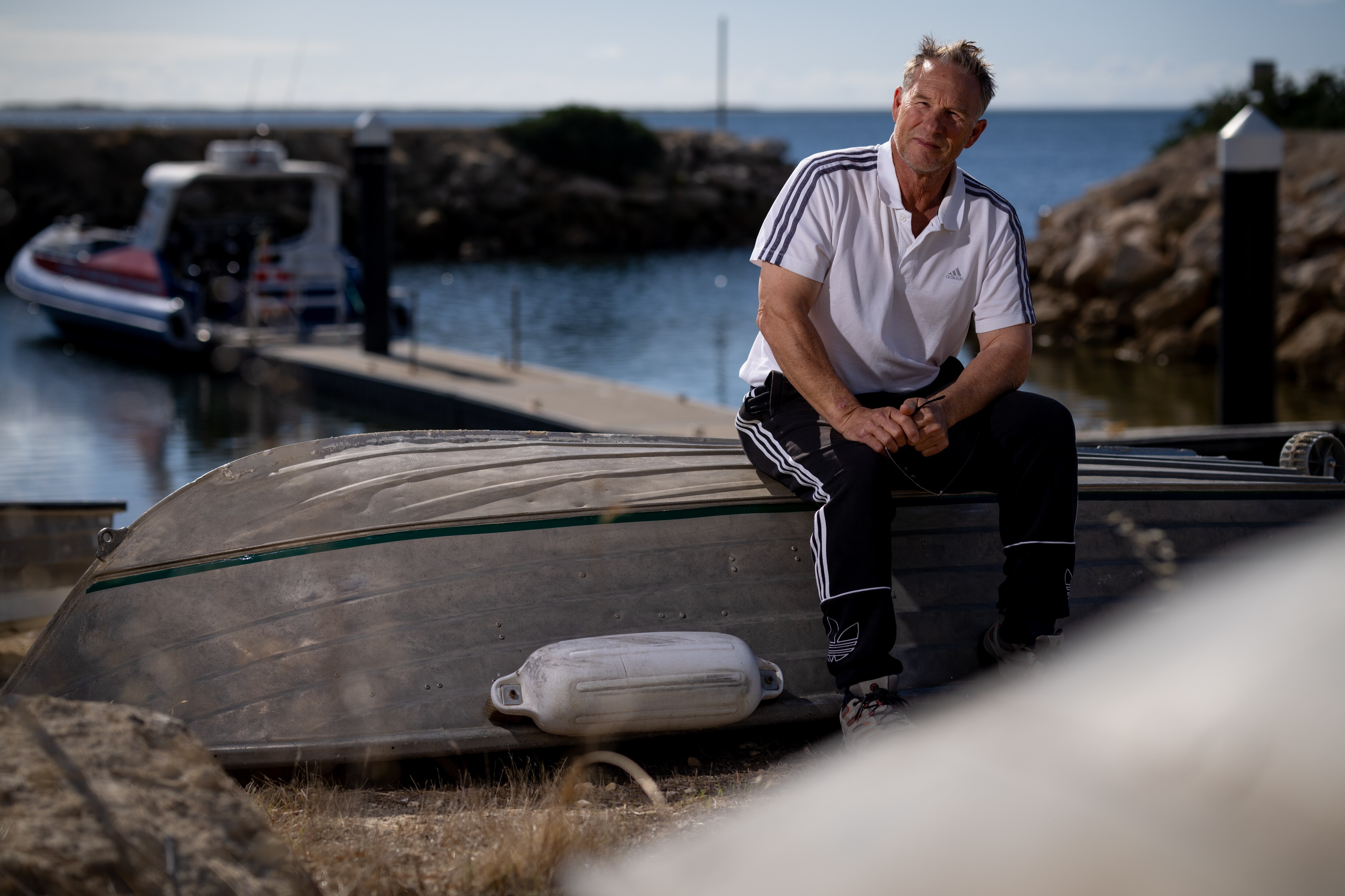 Un pescador se sienta en el casco de un bote de madera.