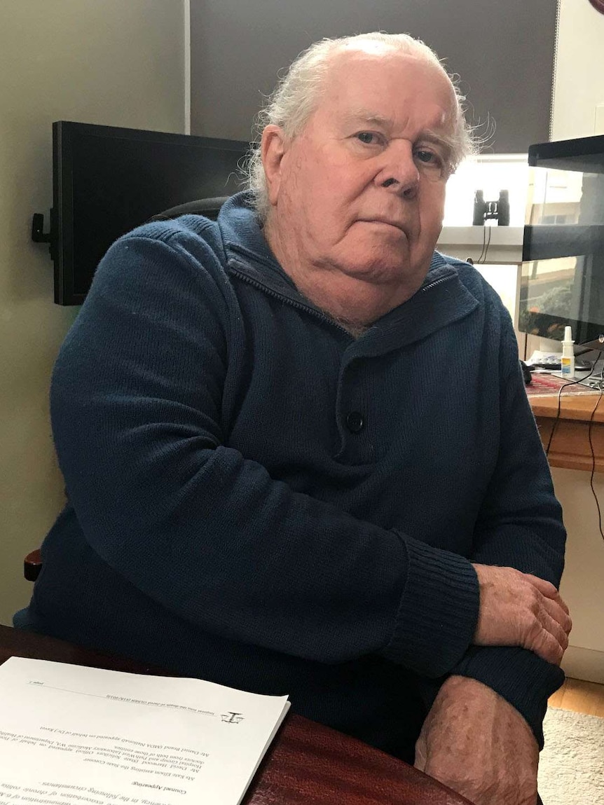 Philip Olsen looks at the camera sitting at a kitchen table with computer screens in the background.