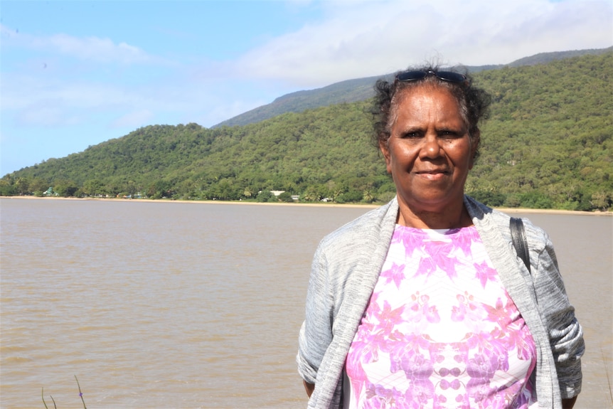 Indigenous Elder stands on the coastline with the mountains and the sea in the background