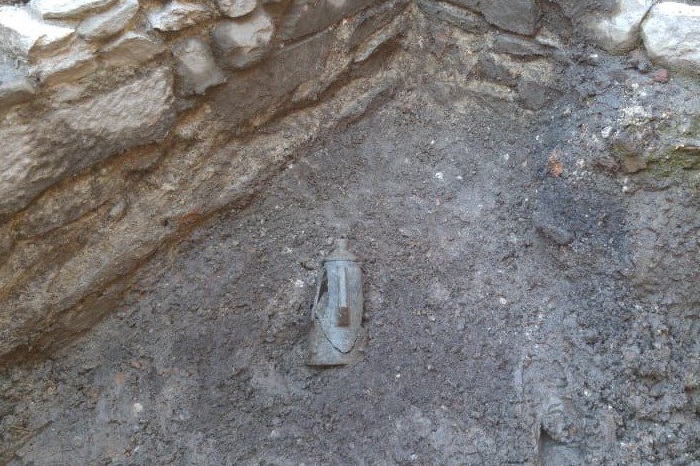 An ancient stone jar lies half buried in the dirt of an excavation site