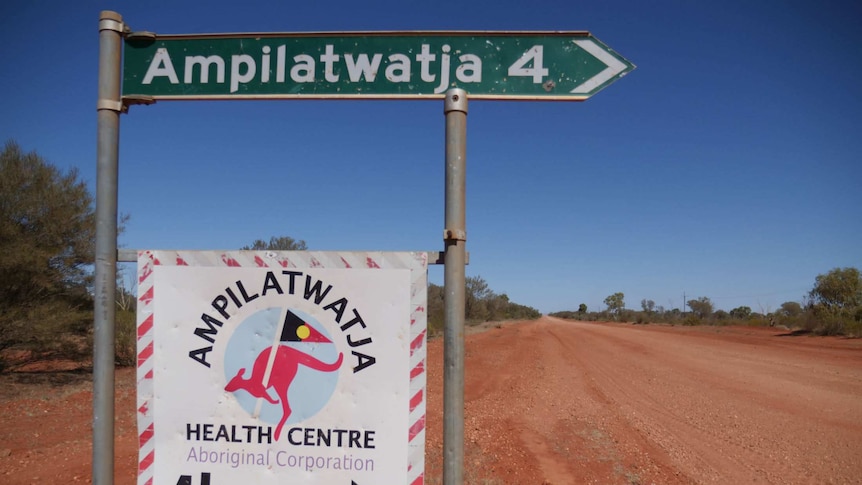 A road sign pointing right with the symbol for 4km alongside a wide, red dirt road.