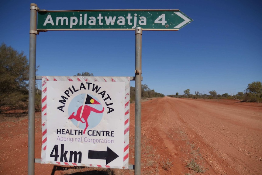 A road sign pointing right with the symbol for 4km alongside a wide, red dirt road.