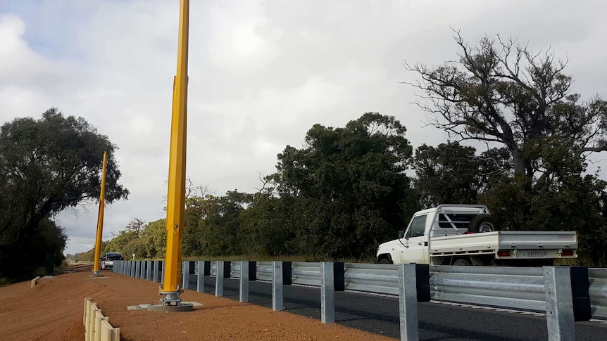 A ute drives past yellow speed camera poles.
