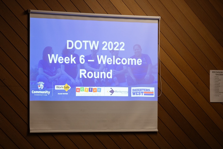 A slide on a projector reads 'DOTW 2022 Week 6 - Welcome Round'