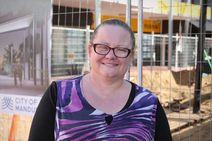 A woman in a purple dress stands in front of a construction fence