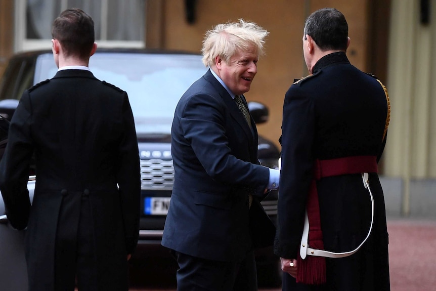 British Prime Minister Boris Johnson smiles and shakes hands with a man in military garb outside Buckingham Palace.