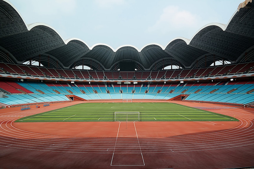 An ultrawide colour photograph of a athletics track and soccer pitch inside Rungrado May Day Stadium in Pyongyang on a clear day