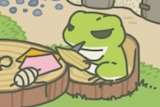 A screen shot from the game Travel Frog. The frog is sitting at a table carving a piece of wood.