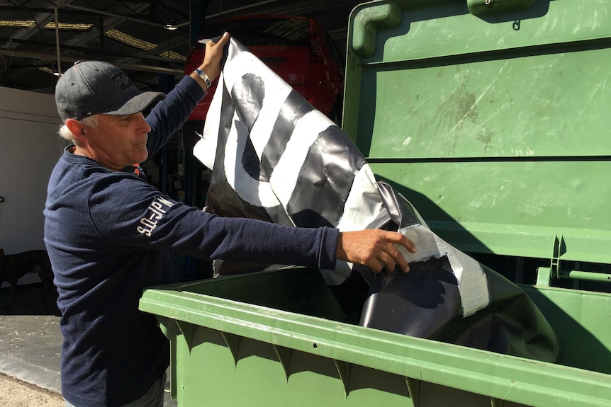 A man holds a 'Vote Tony Abbott' sign over a big industrial bin.