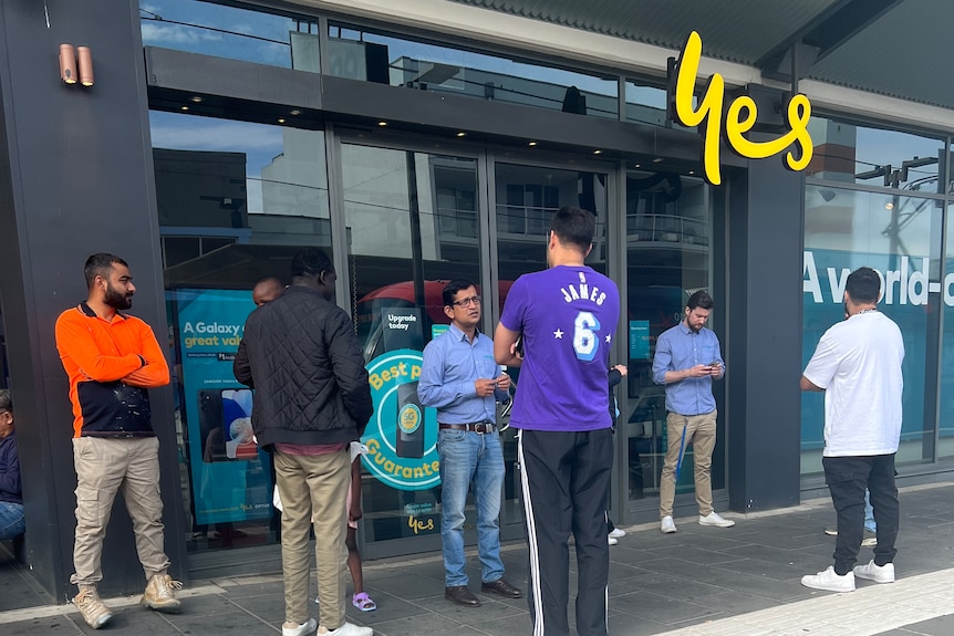 A crowd of people stand on the street outside an Optus store