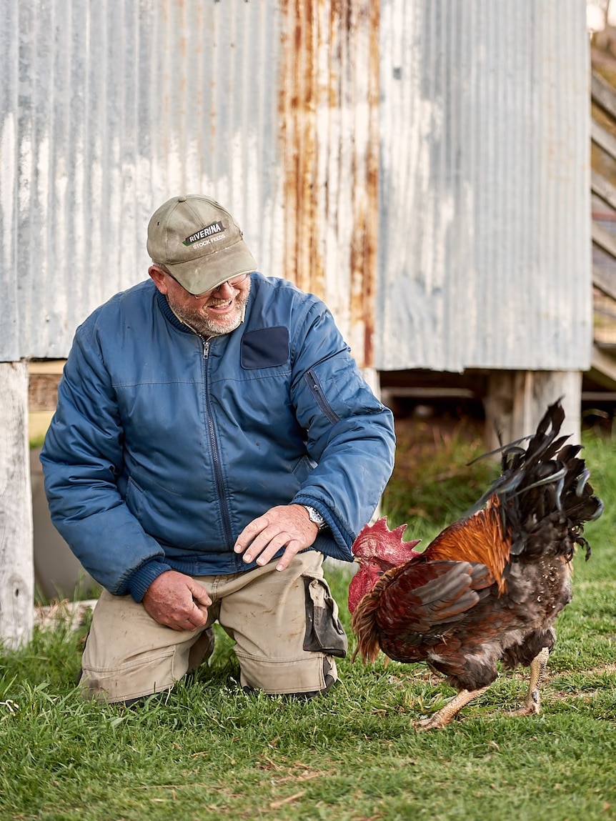 An older man in front of a shed with a rooster