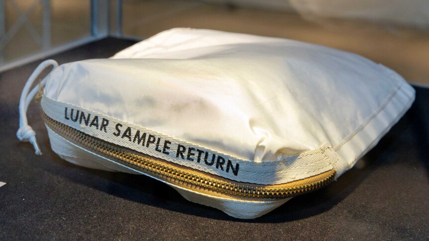 A white, zippered fabric bag with 'Lunar Sample Return' written on it sits on a table.