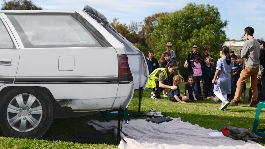 A tent that looks like a car on grass with people in the background