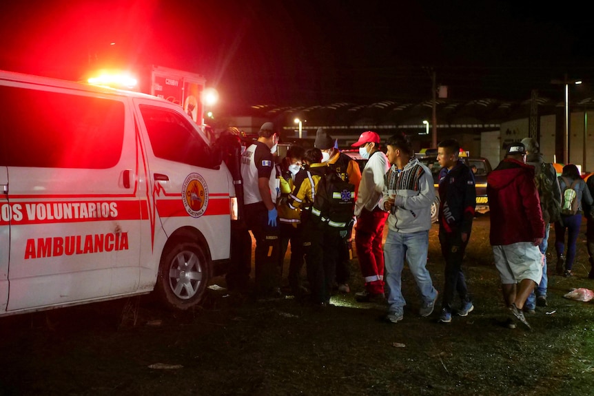 Ambulance at scene of crowd crush, as people stand beside vehicle.