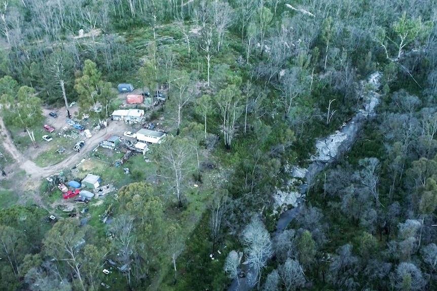 An aerial shot of a property with several sheds and cars in the forest