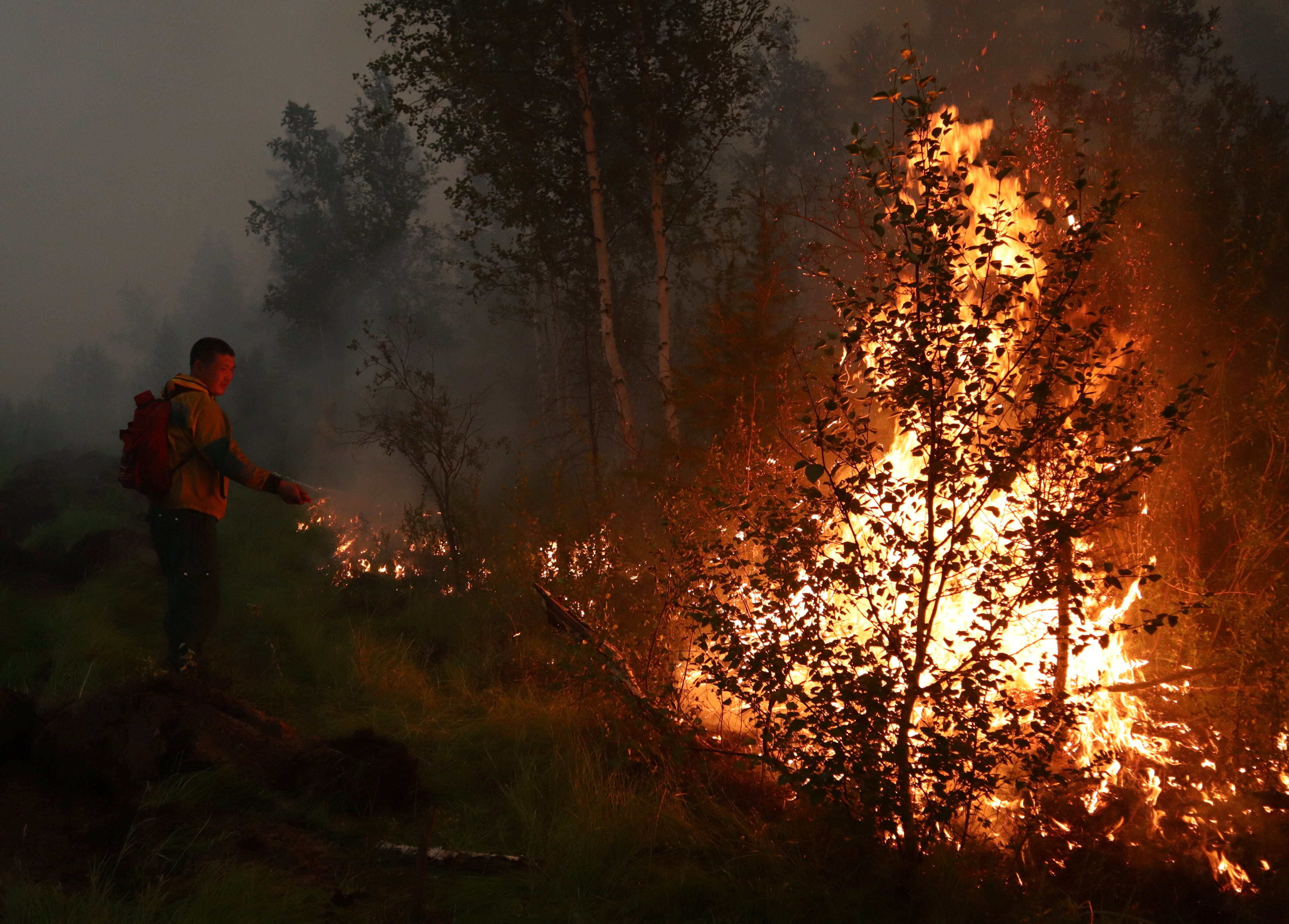 A firefighter tries to extinguish a wall of flames