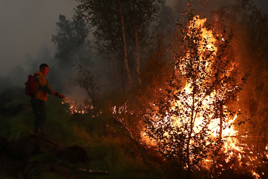 A firefighter tries to extinguish a wall of flames