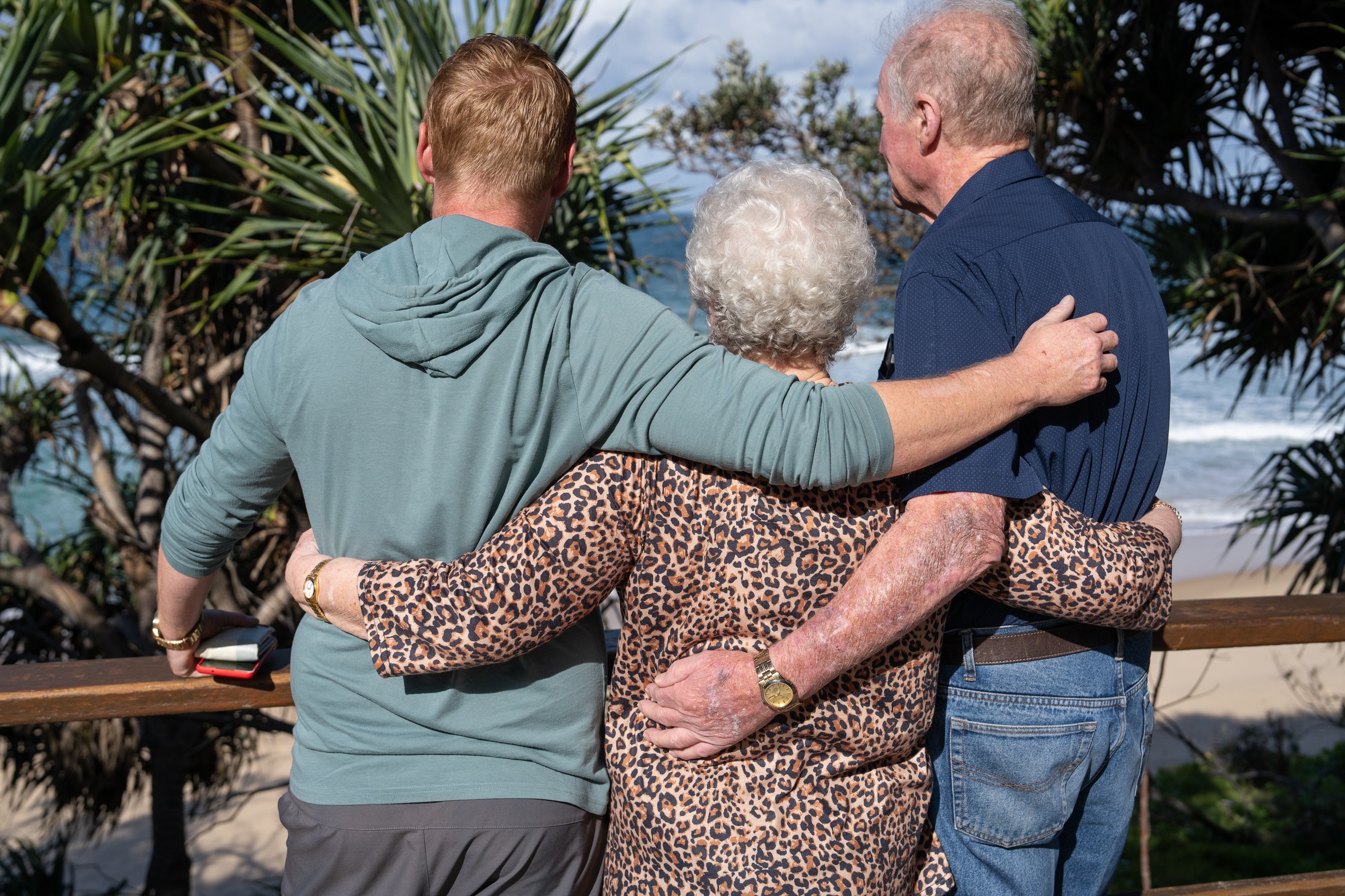 Three people stand with their backs to the camera and their arms around one another.