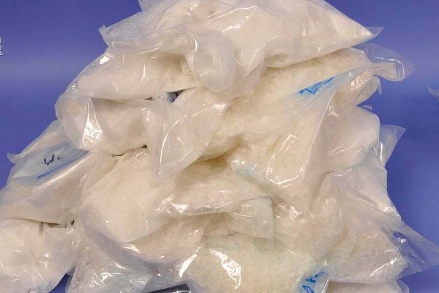 Gros plan d'une pile de sacs en plastique transparent remplis de drogues illégales de couleur blanche.