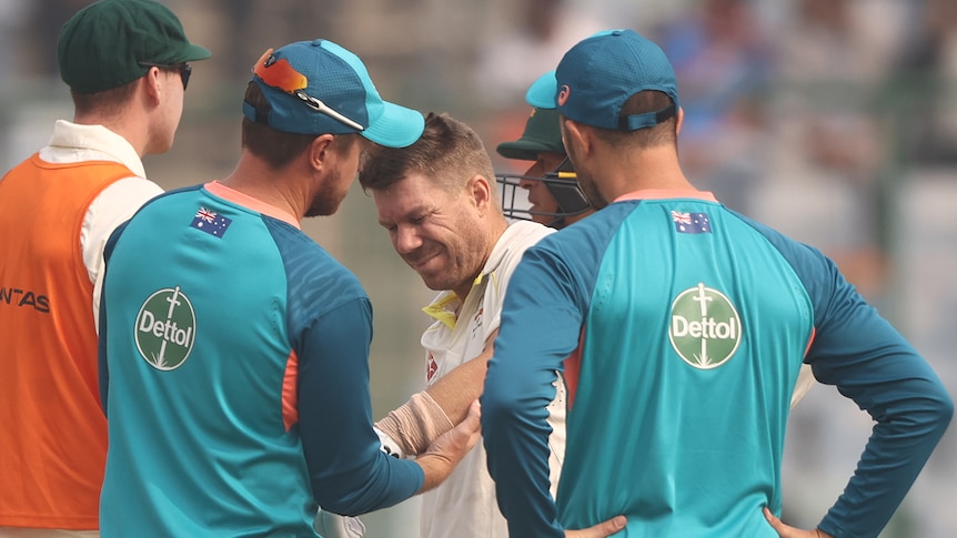 An Australian male batter receives medical attention on the field during a Test match in Delhi.