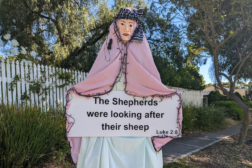 A tall statue dressed as a shepherd holding a sign on a street verge