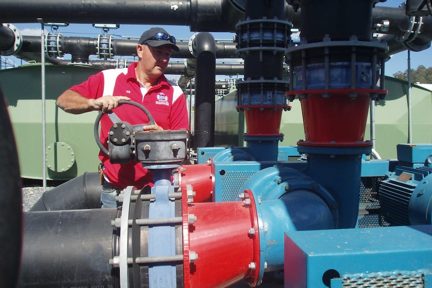 Man in red shirt with hands on the steel wheel controlling a water valve