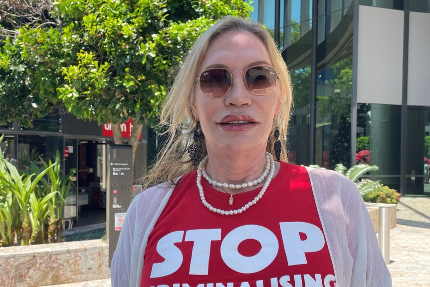 Elle Coles wears sunglasses and a red shirt that reads "stop criminalising sex worker safety"